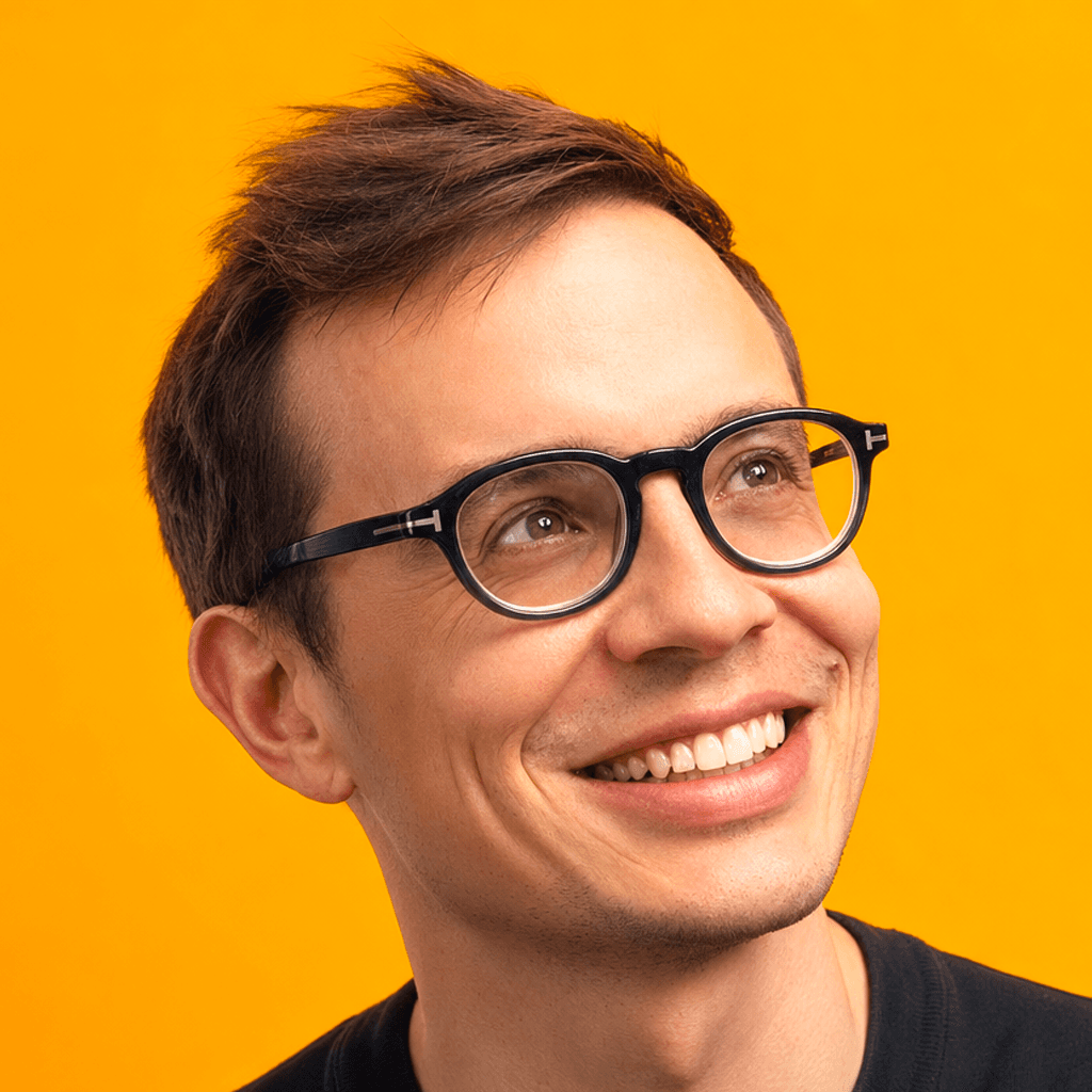 Ilias Ism smiling, short brown hair, black glasses, navy t-shirt, yellow background