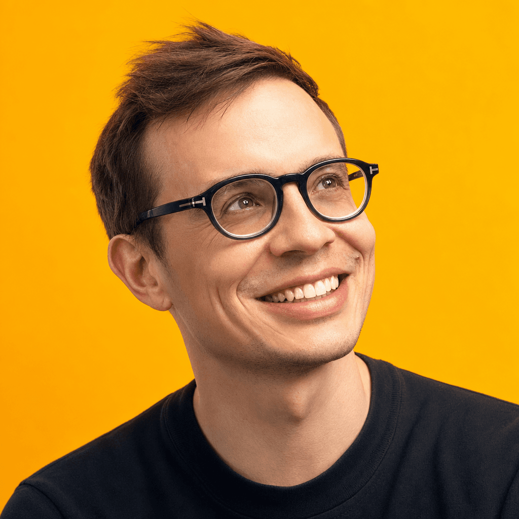 Ilias Ism smiling, short brown hair, black glasses, navy t-shirt, yellow background
